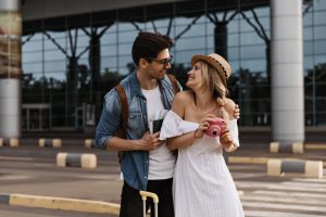 blonde-woman-hat-white-dress-smiles-looks-boyfriend-holds-pink-camera-min